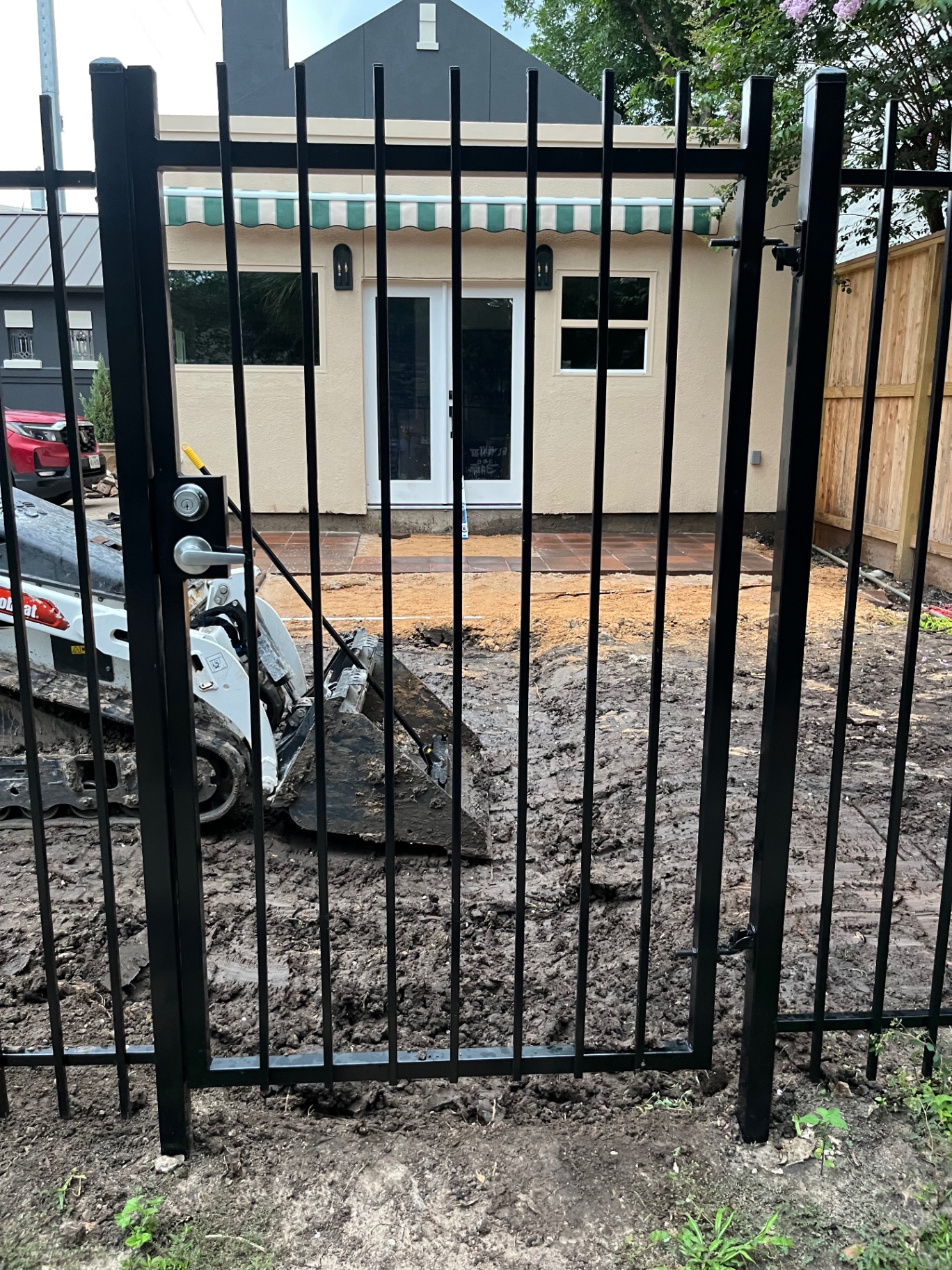 Before — muddy construction site with excavator behind a black metal fence